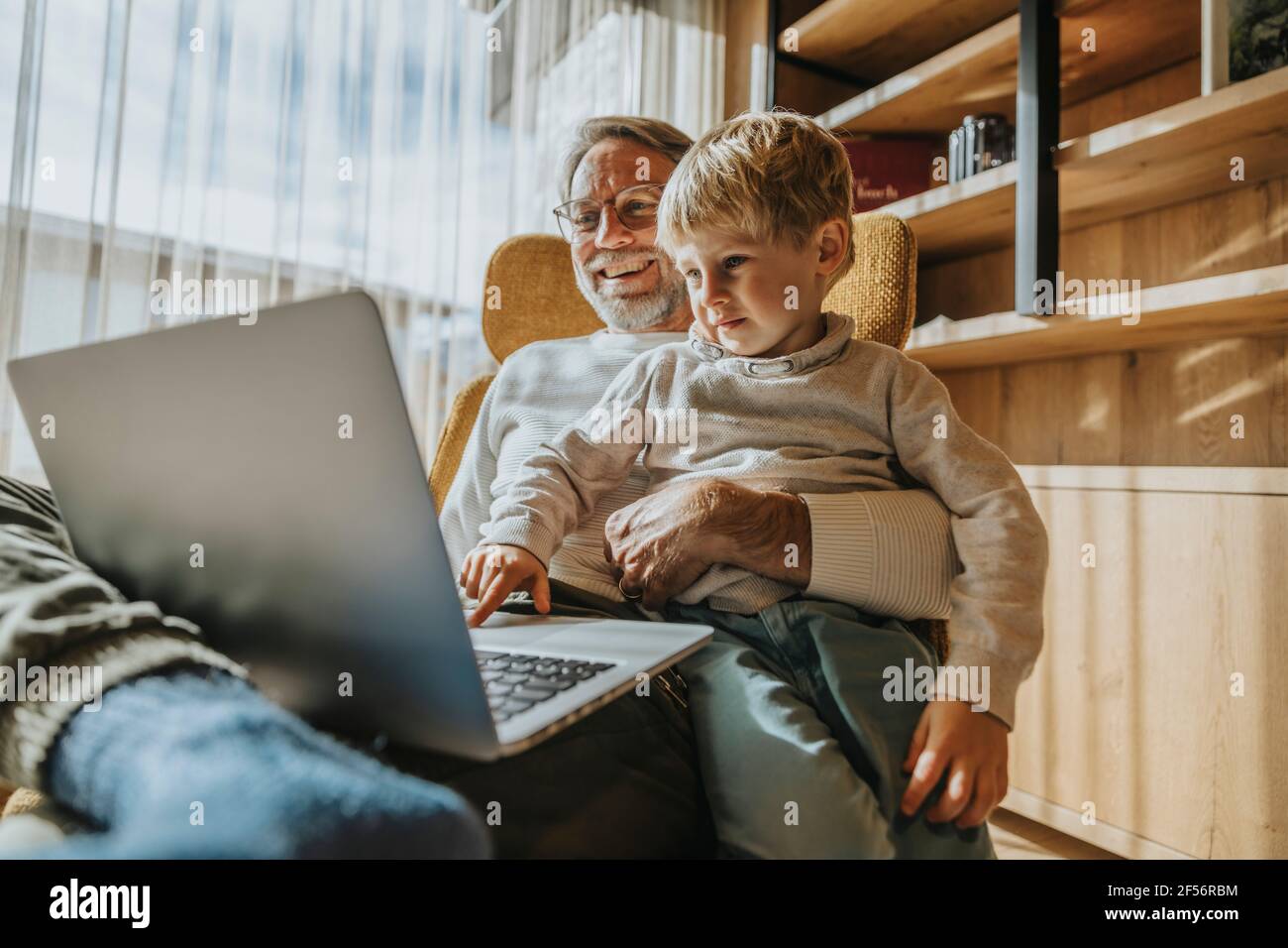 Boy using laptop while sitting with father on chair Stock Photo