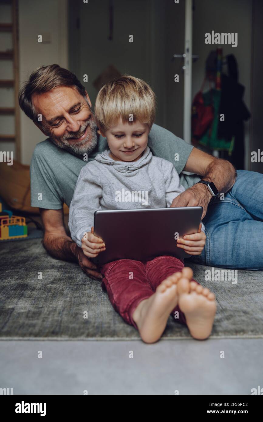 Smiling father watching son using tablet in bedroom Stock Photo