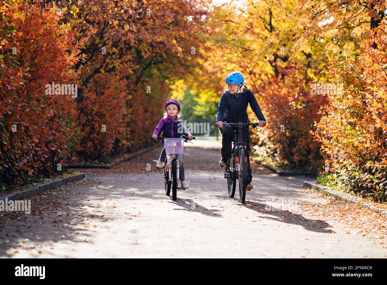 Cheerful mother and daughter cycling in park during autumn Stock Photo