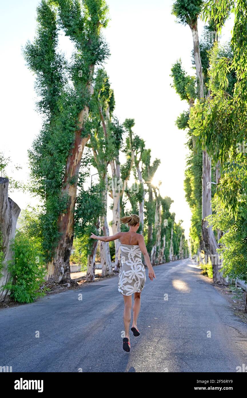 Greece, Dodecanese, Kolymbia, Adult woman hopping merrily along eucalyptus avenue in summer Stock Photo