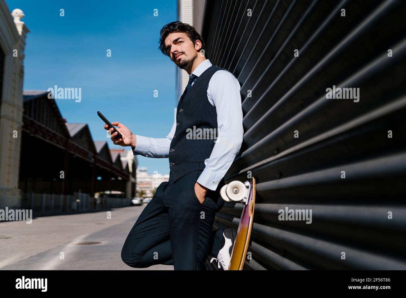 Businessman looking away while holding mobile phone against wall Stock Photo