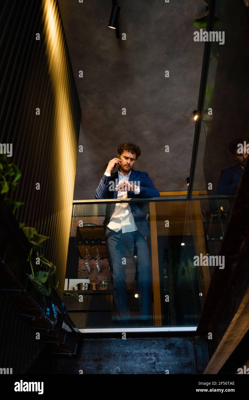 Businessman checking time while talking on smart phone at cafe Stock Photo
