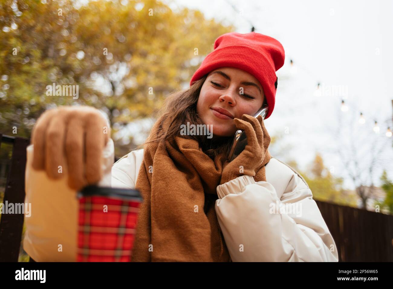 Woman wearing warm clothing talking on smart phone while sitting at sidewalk cafe Stock Photo
