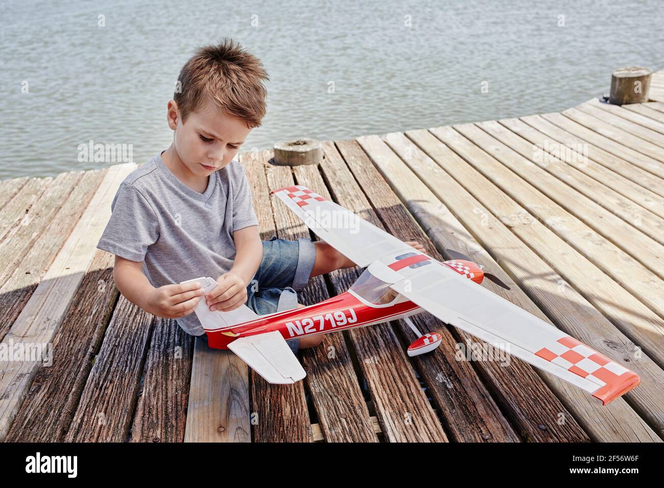 Boy checking airplane toy while sitting on pier Stock Photo