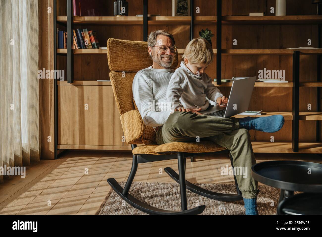 Boy using laptop while sitting with father on chair Stock Photo