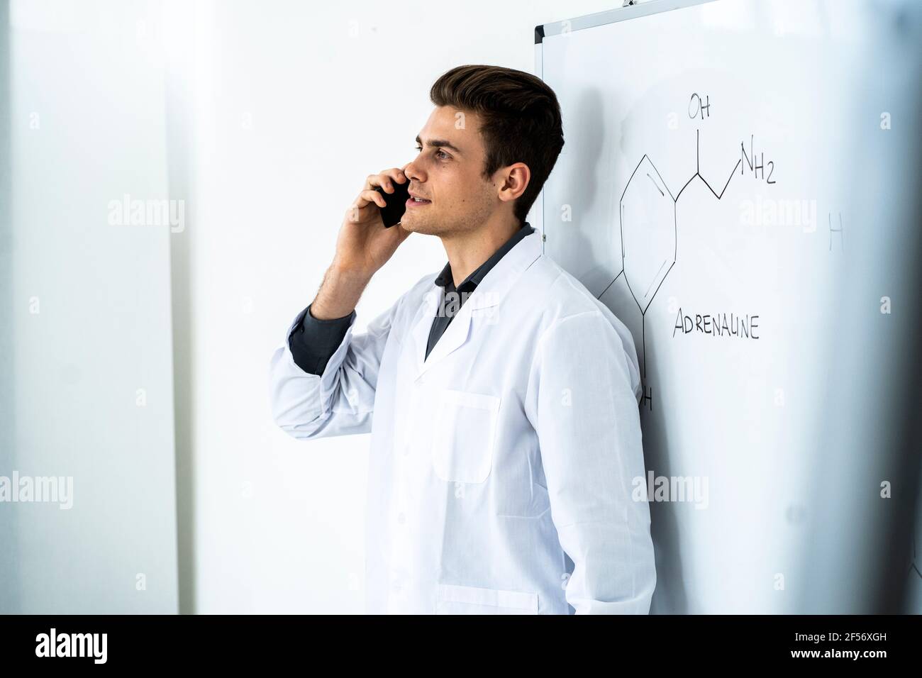 Young male scientist talking on smart phone while standing against whiteboard in laboratory Stock Photo