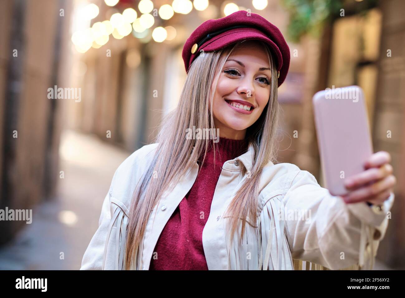 Smiling beautiful woman wearing flat cap taking selfie through smart phone Stock Photo