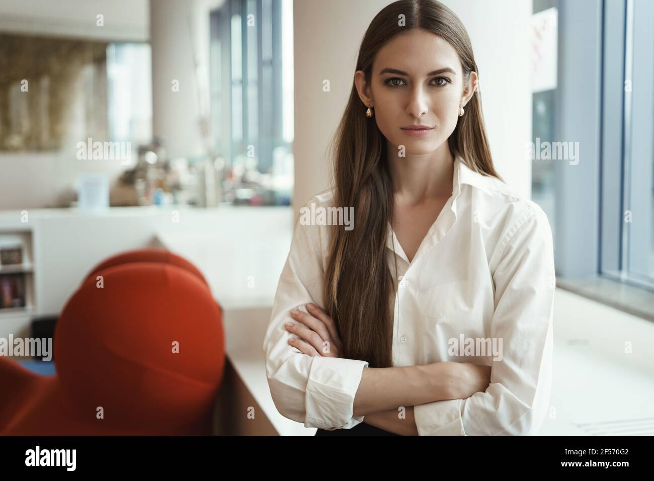 Successful young businesswoman standing in co-working space, looking confident, showing readiness taking action. Empowered female entrepreneur cross Stock Photo
