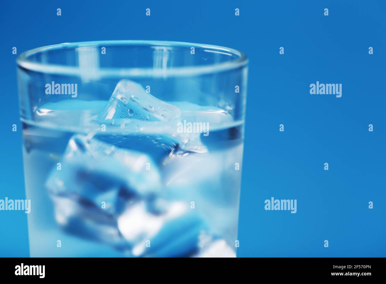 A glass with ice water and ice cubes on a blue background. A refreshing ...