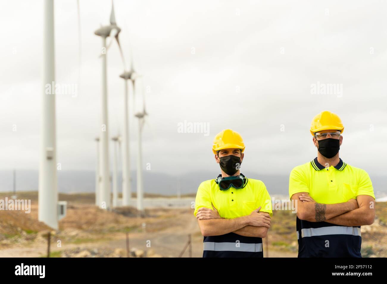 Front view of two skilled workers in a wind turbine power station. Two male electrician workers in reflective vests and hard hats. Clean energy. Stock Photo
