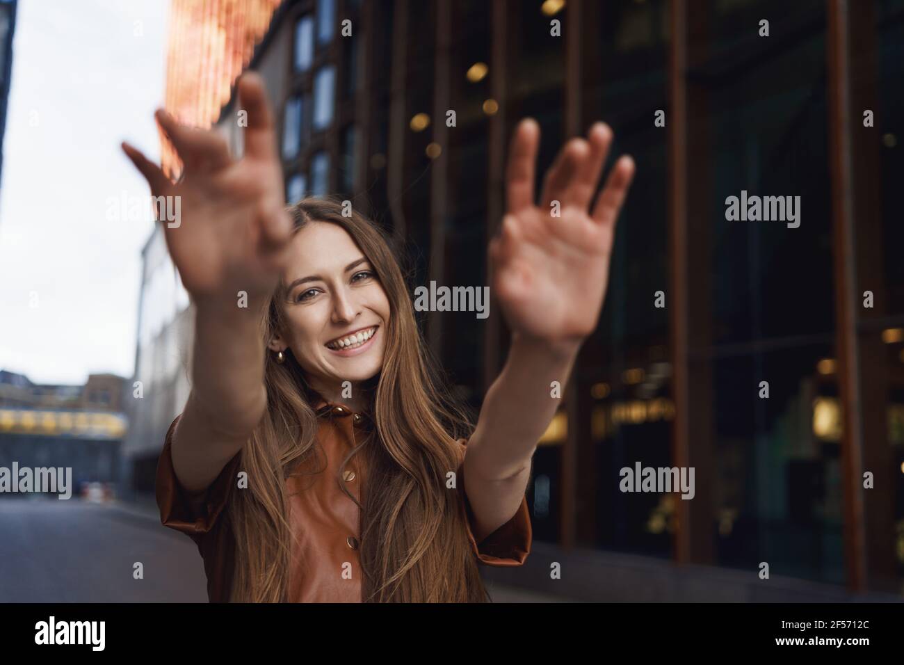 Girl catching her dreams. Alluring happy smiling woman reaching hands at camera and laughing while walking along street with joyful, upbeat feeling in Stock Photo