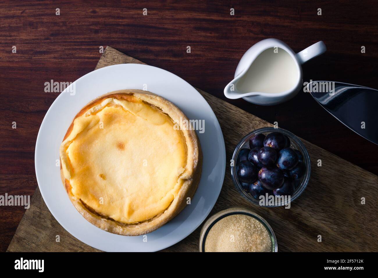 Grandma's cheesecake besides grapes and cane sugar on dark wooden board Stock Photo