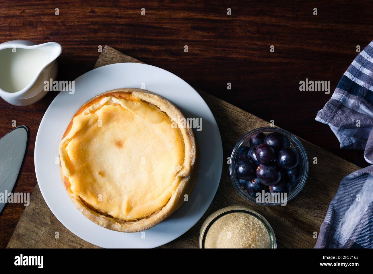 Grandma's homemade cheesecake besides grapes and milk and sugar on dark wooden board Stock Photo