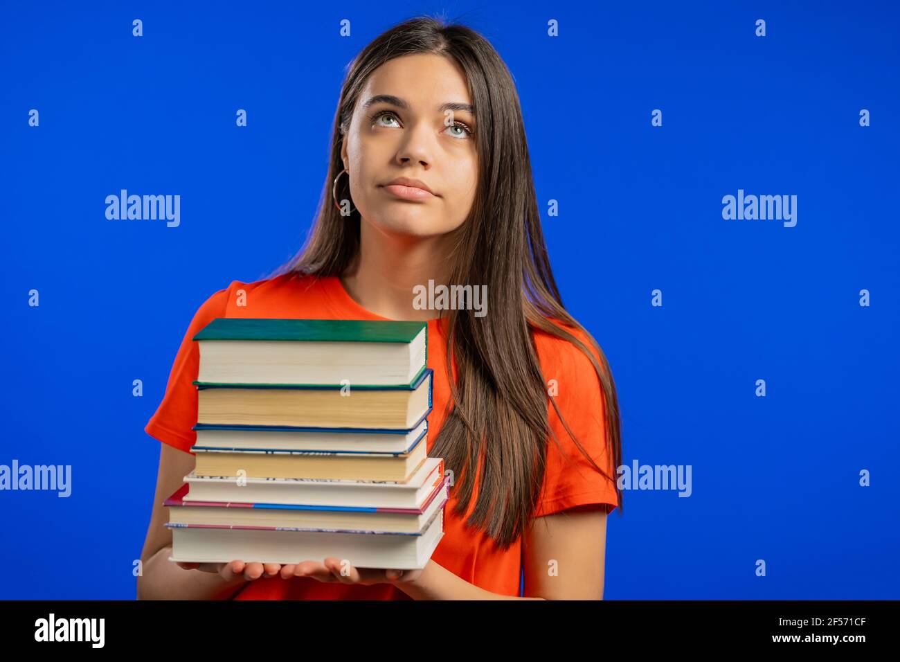 Bored woman is dissatisfied with amount of homework and books. Lady is annoyed, discouraged frustrated by studies. Blue studio background  Stock Photo