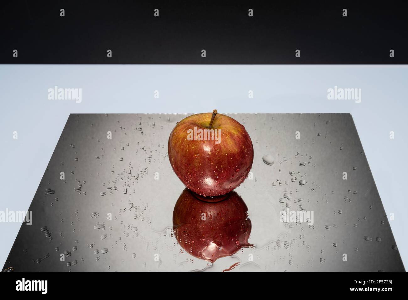 A red apple resting on a mirror with falling water drops Stock Photo