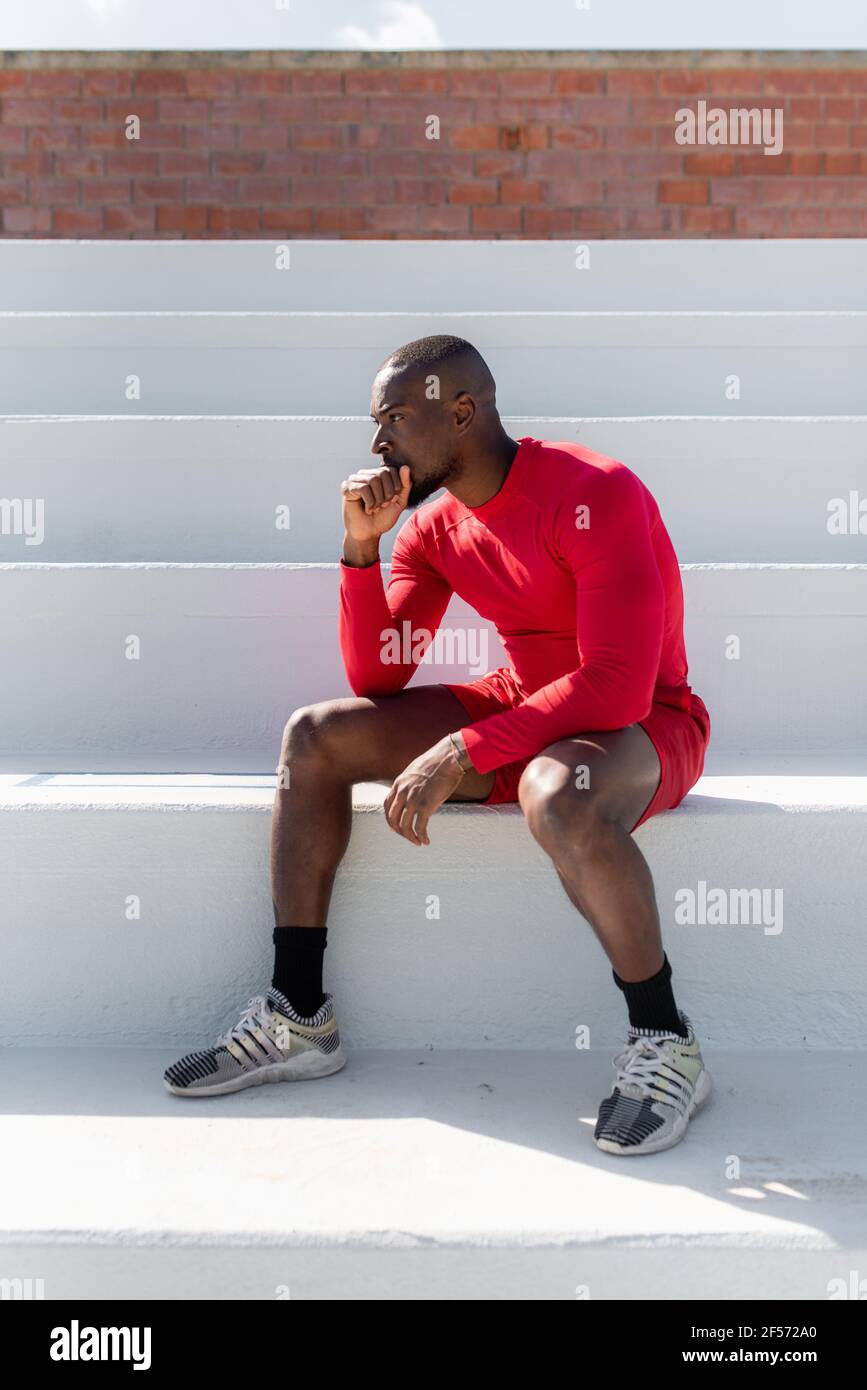 Side view athletic black sportsman sitting on stairs resting chin on hand looking ahead with serious focused face. Stock Photo