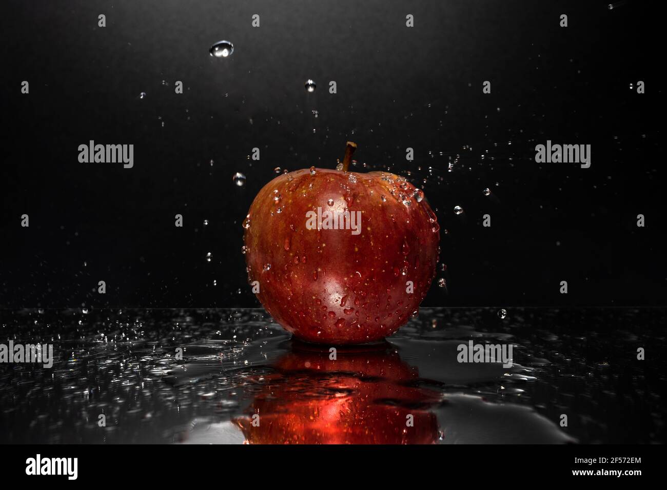 A red apple resting on a mirror with falling water drops Stock Photo