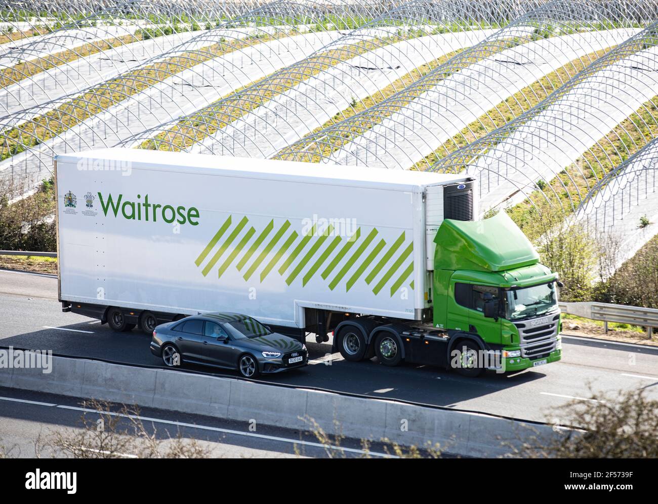A Waitrose delivery lorry heads down the motorway passed fields of poly tunnels in the sunshine Stock Photo