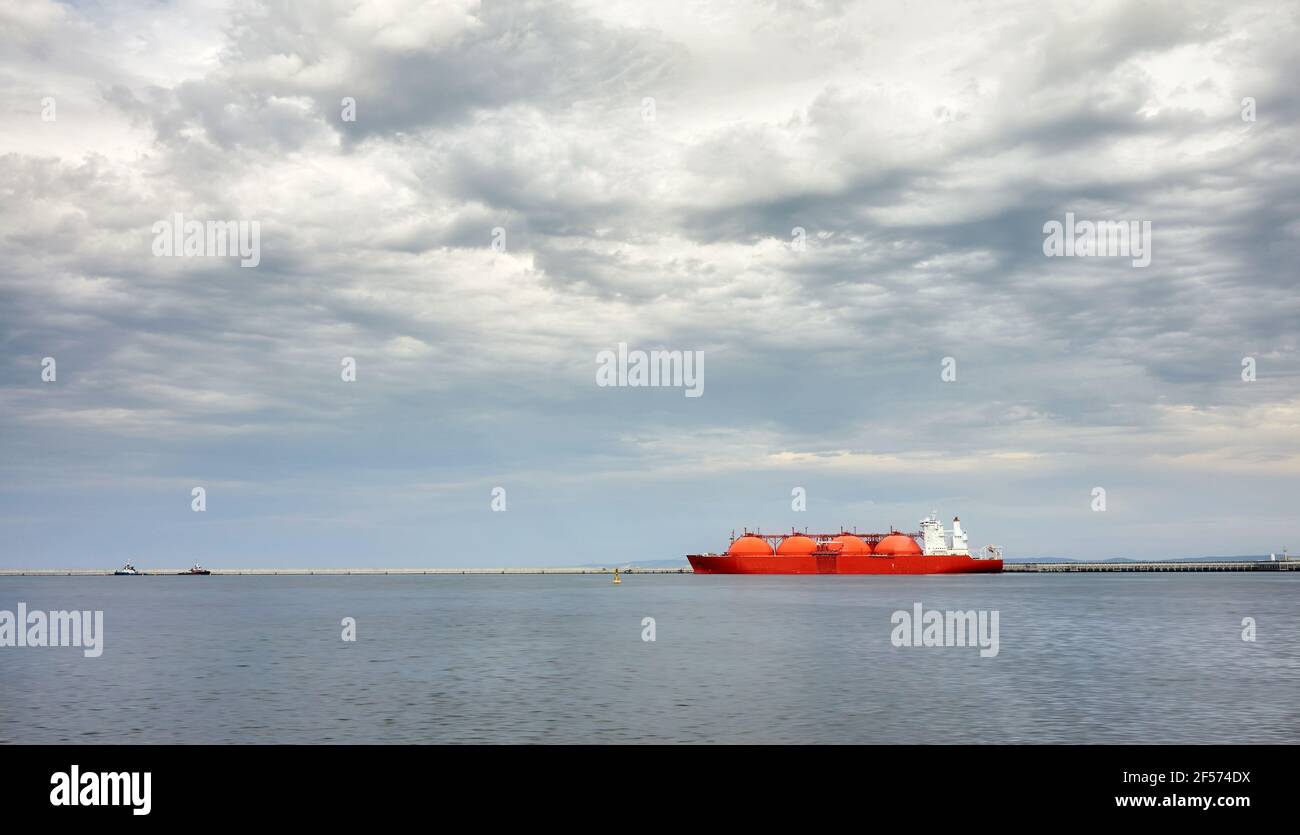 Red LNG tanker in port with stormy cloudscape. Stock Photo