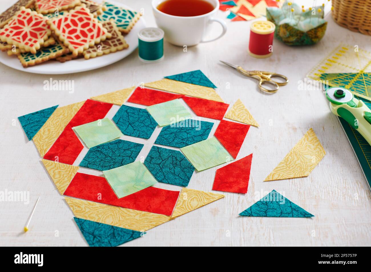Pieces of fabric laid out in the shape of a patchwork block, a  heap of cookies with a pattern imitating a patchwork block, a cup of tea, sewing and q Stock Photo