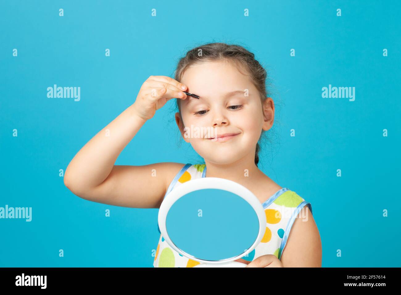 close-up portrait of a girl in a white dress combing her eyebrows with a brush and making up, isolated on a blue background Stock Photo