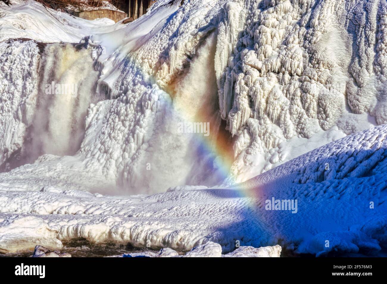 A rainbow caused by the spring thaw starting at the frozen Chutes de la Chaudière in Quebec City, Canada Stock Photo