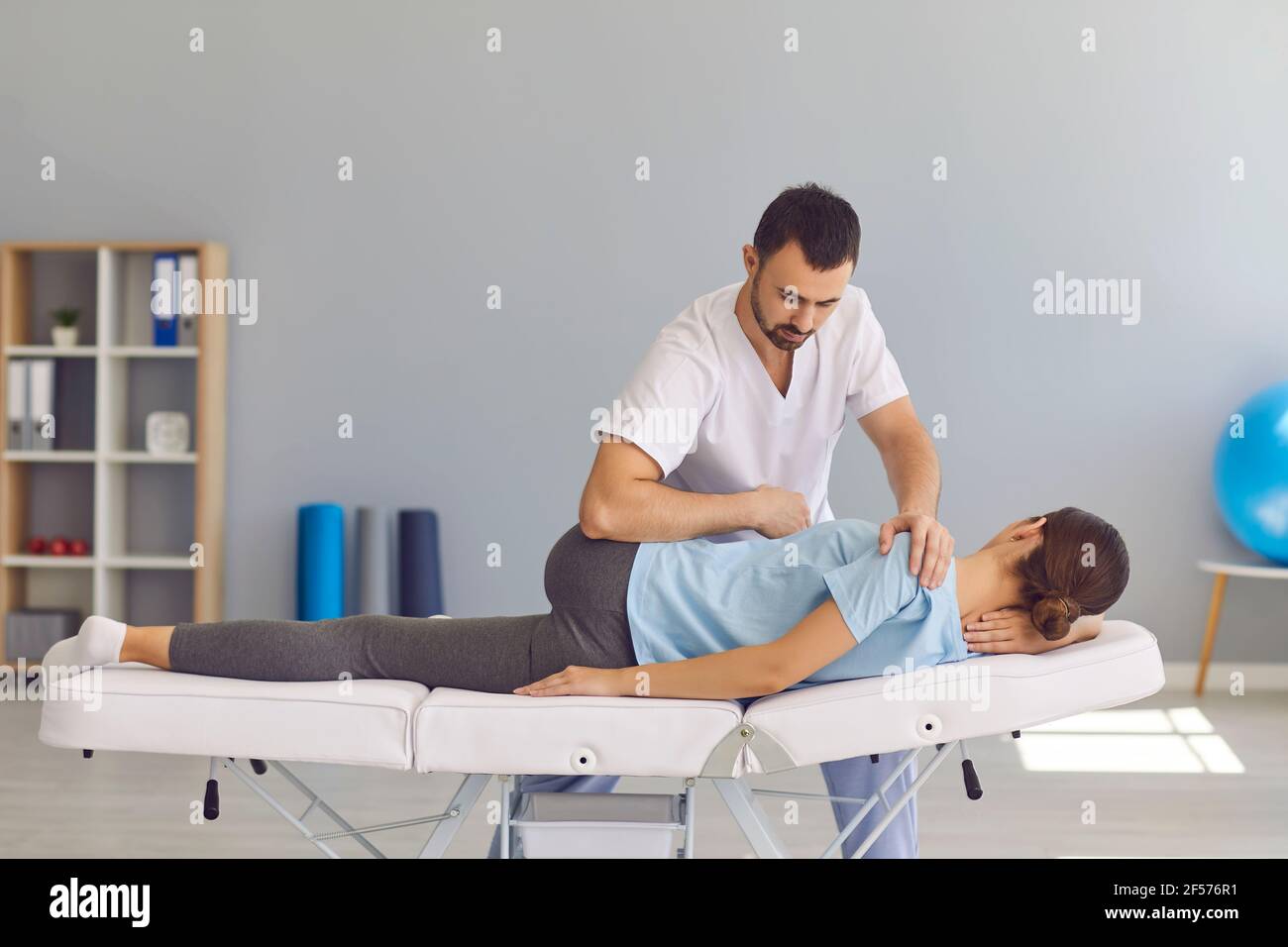 Confident man doctor chiropractor or osteopath fixing womans back and legs joints Stock Photo
