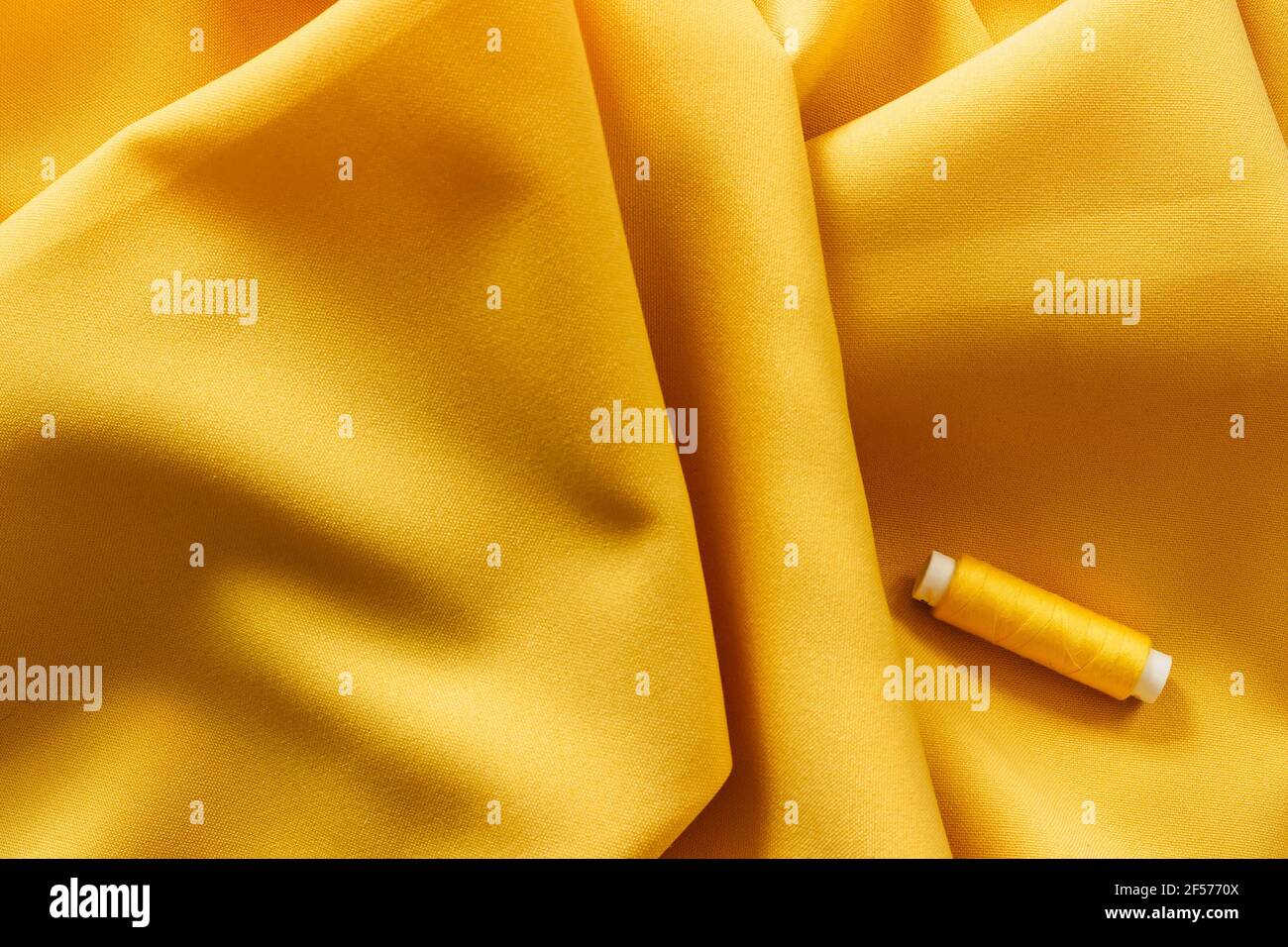 Yellow fabric texture and sewing thread.Spring color.Abstract yellow background. Smooth elegant golden textile. Trendy Color of the Year 2021. Color Stock Photo