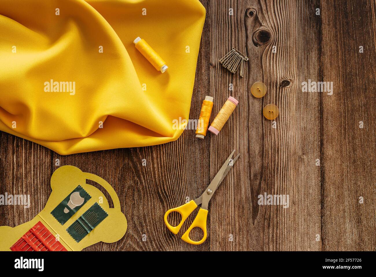 Sewing accessories and yellow fabric on wooden table. Sewing threads, needles, pins, buttons and scissors. Top view, flat lay concept. Accessories Stock Photo