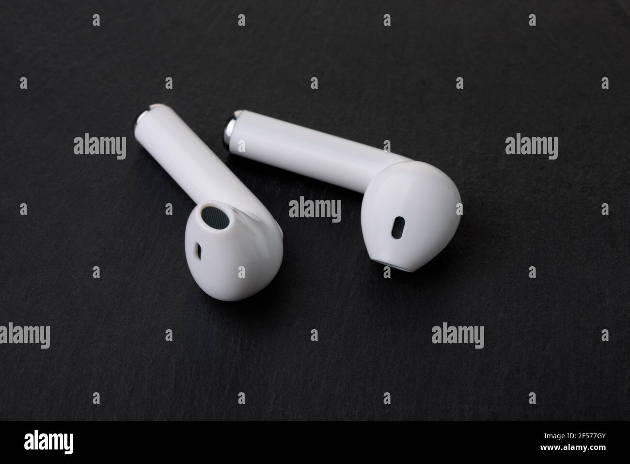 Pair of white true wireless earbuds on black stone background Stock Photo