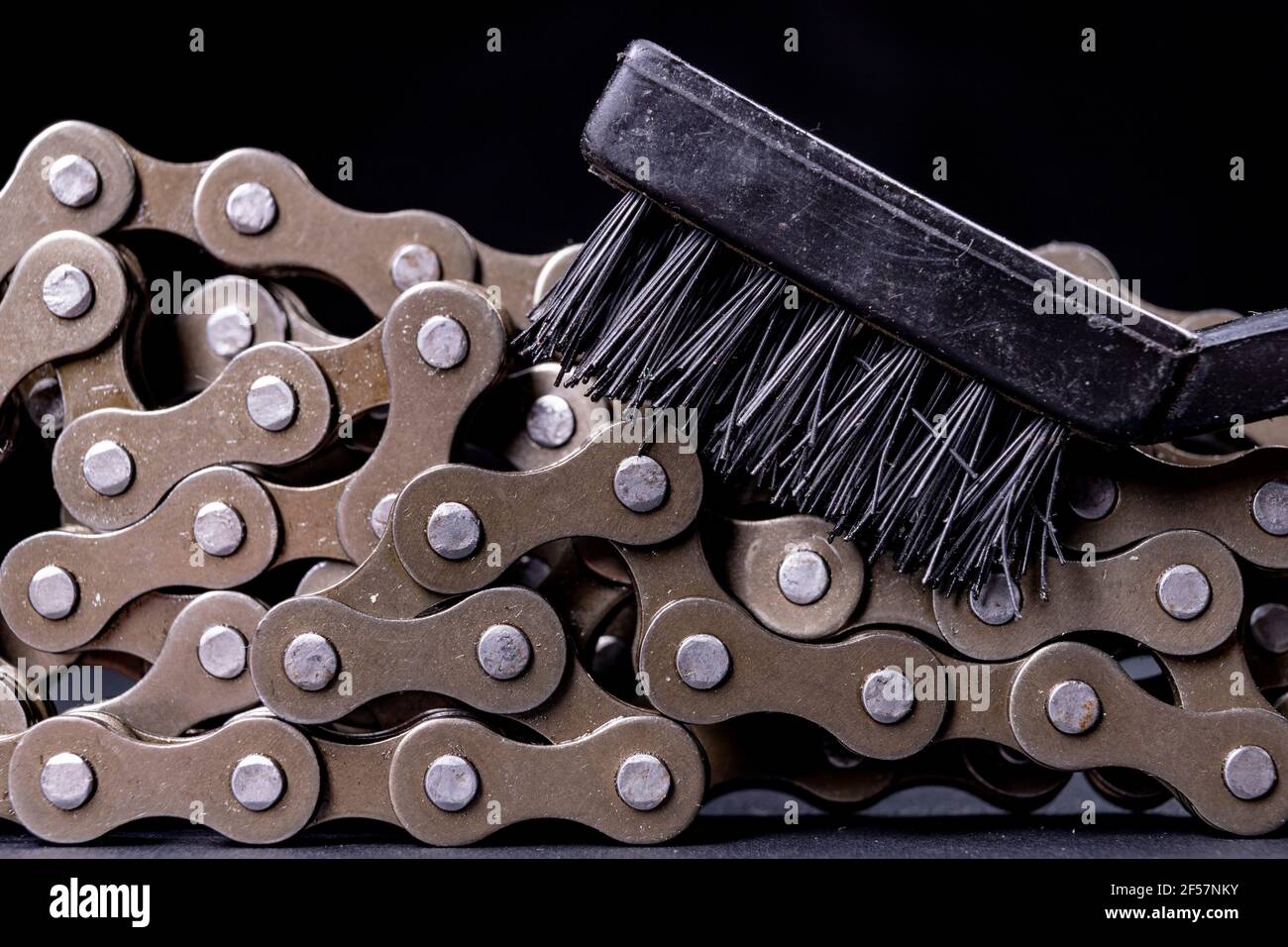 Cleaning the bicycle chain with a plastic brush. Maintenance work carried out in a bicycle workshop. Dark background. Stock Photo