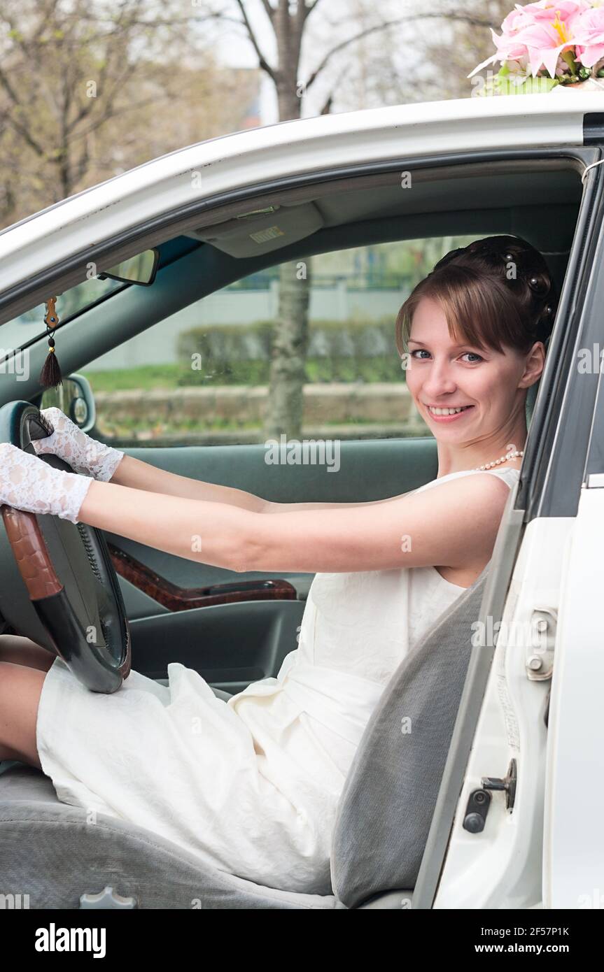 Smiling bride wearing white dress and gloves sitting on driver seat in