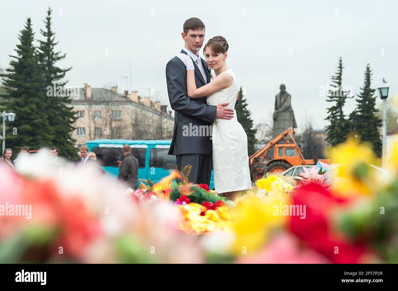 Russian bride and groom standing and embracing near memorial with eternal fire and flowers in a city center. Petrozavodsk, Russia Stock Photo