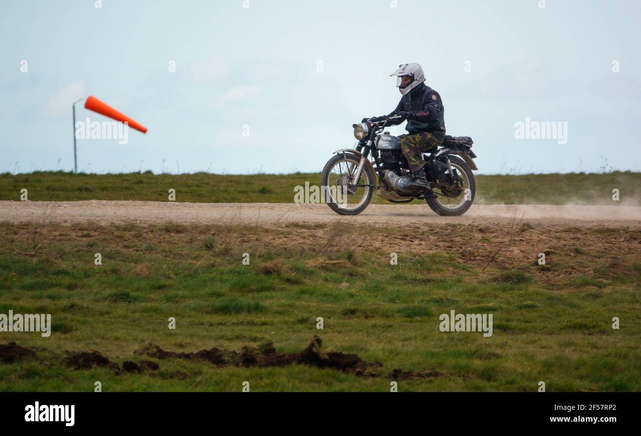 a motorcyclist rides his classic Royal Enfield four stroke motorbike along a dusty stone track over Salisbury Plain Stock Photo