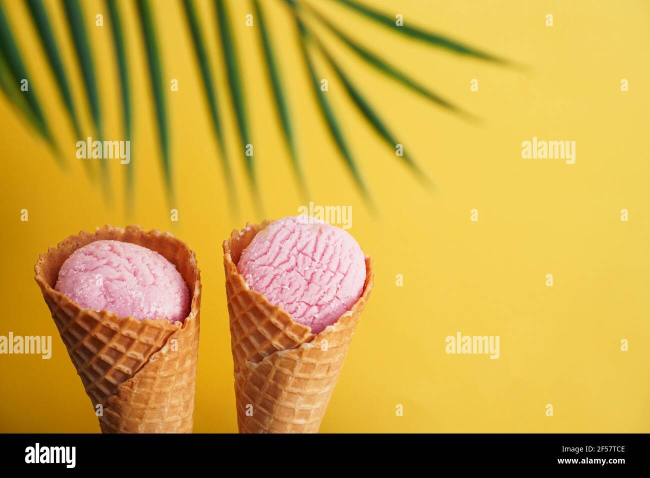 Two strawberry ice creams in a cone on a yellow background. Tropical