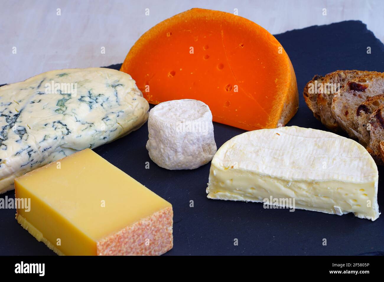 Cheese platter with comte,fourme,goat cheese crottin, camembert and orange mimolette cheese on a slate board Stock Photo