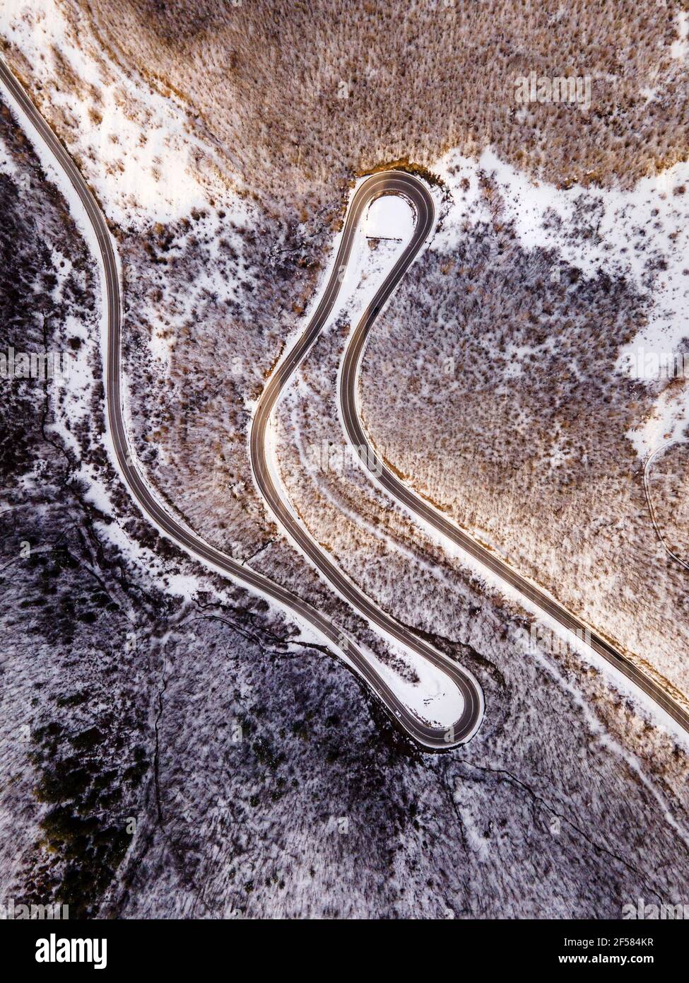High angle aerial view drone image on the curved serpentine road trough the trees and forest in mountain range with white snow in winter day near Knja Stock Photo