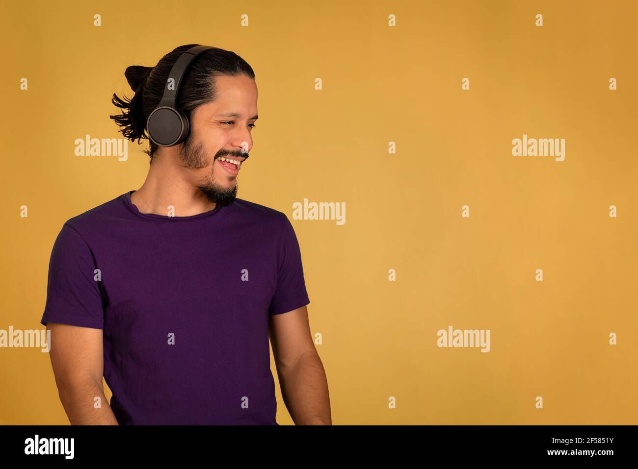 Young man smiling and listening music using headphones. Yellow background. Stock Photo