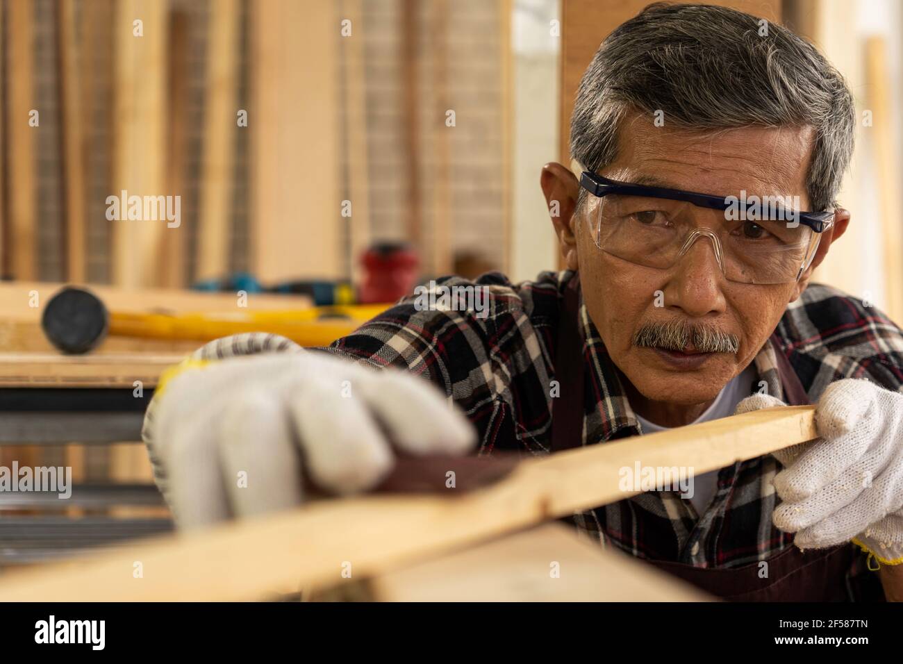 Older worker wearing cloth gloves holds sandpaper to sanding the wood