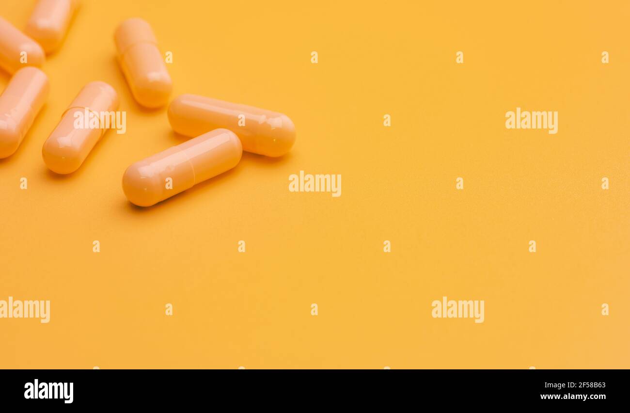 Yellow capsule pills on yellow background with space. Pharmacy and health insurance concept. Prescription drug. Pharmaceutical industry. Vitamins. Stock Photo