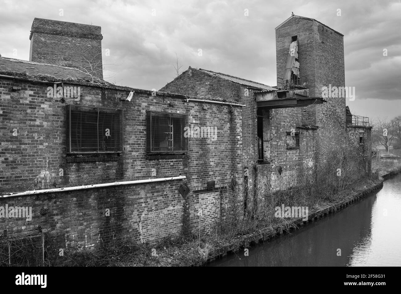 A black and white photograph showing urban decay. An old neglected building abandoned by the side of a canal Stock Photo