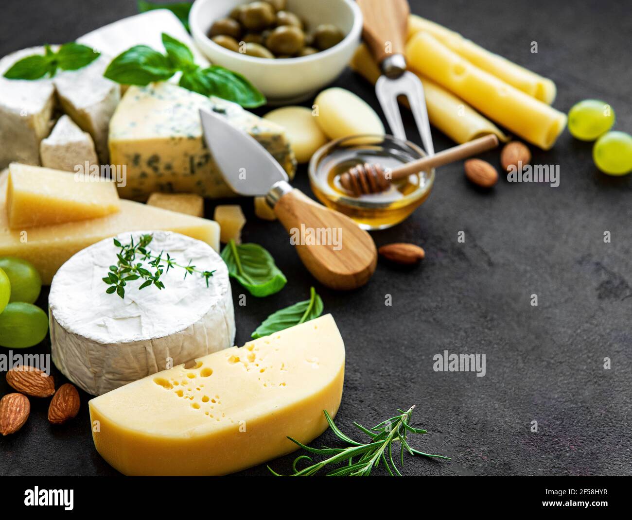 Various types of cheese, grapes, honey and snacks on a black concrete background Stock Photo