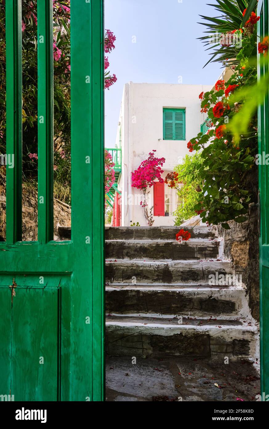 Entrance to traditional Greek island house. Whitewashed walls, pink bougainvillea, red and green storm shutters. Selective focus. Mykonos, Greece. Stock Photo