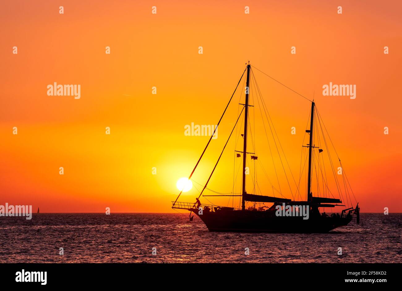 Silhouette of sailing boat with sails down against sun at sunset, sun glare on sea waters. Romantic seascape, sun touch headsail ropes. Stock Photo