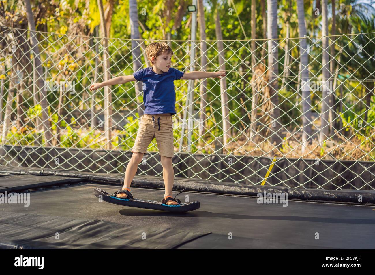 Happy boy on a soft board for a trampoline jumping on an outdoor trampoline, against the backdrop of palm trees. The trampoline board is like a Stock Photo