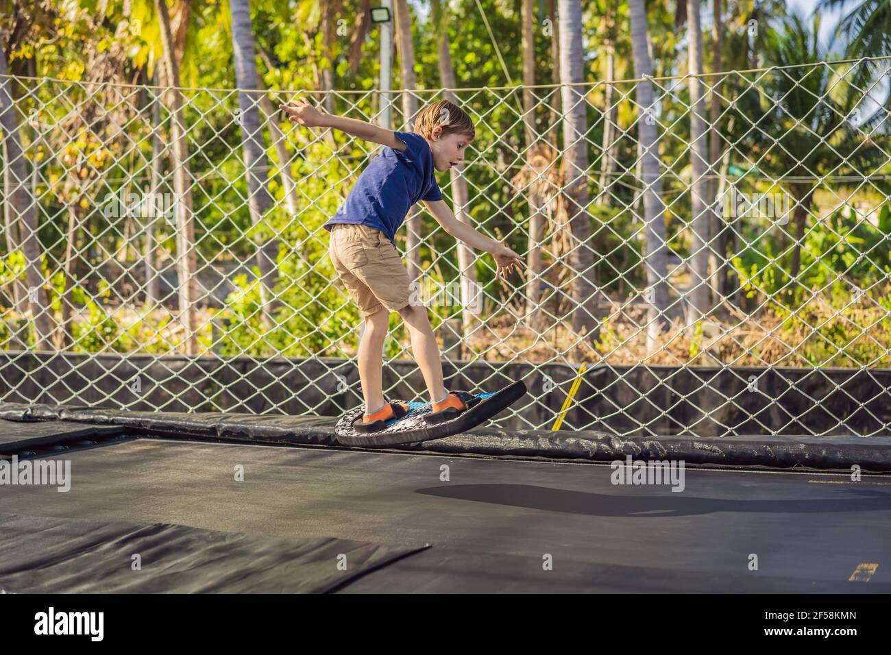 Happy boy on a soft board for a trampoline jumping on an outdoor trampoline, against the backdrop of palm trees. The trampoline board is like a Stock Photo