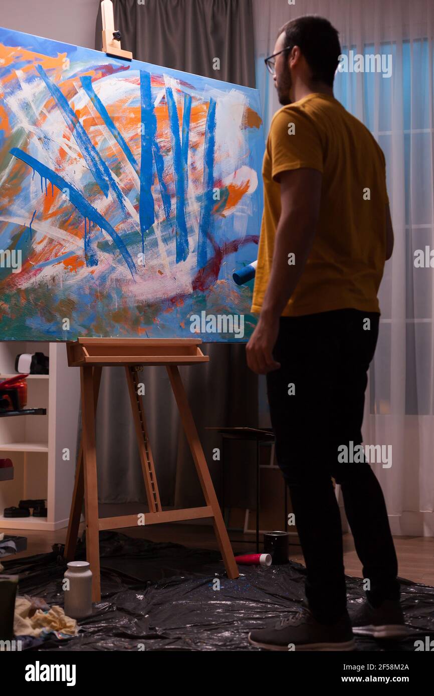 Abstract painter holding roller and looking at his masterpiece painting