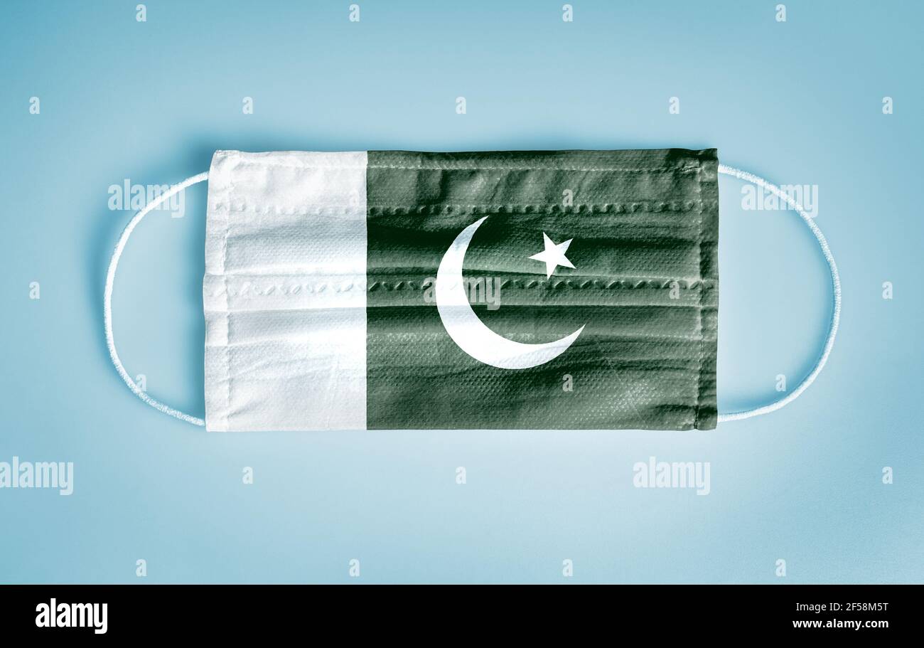 Covid-19 Coronavirus protection concept: Medical disposable face mask with Pakistan flag on blue background.  WHO recommends usage of mask for safety. Stock Photo