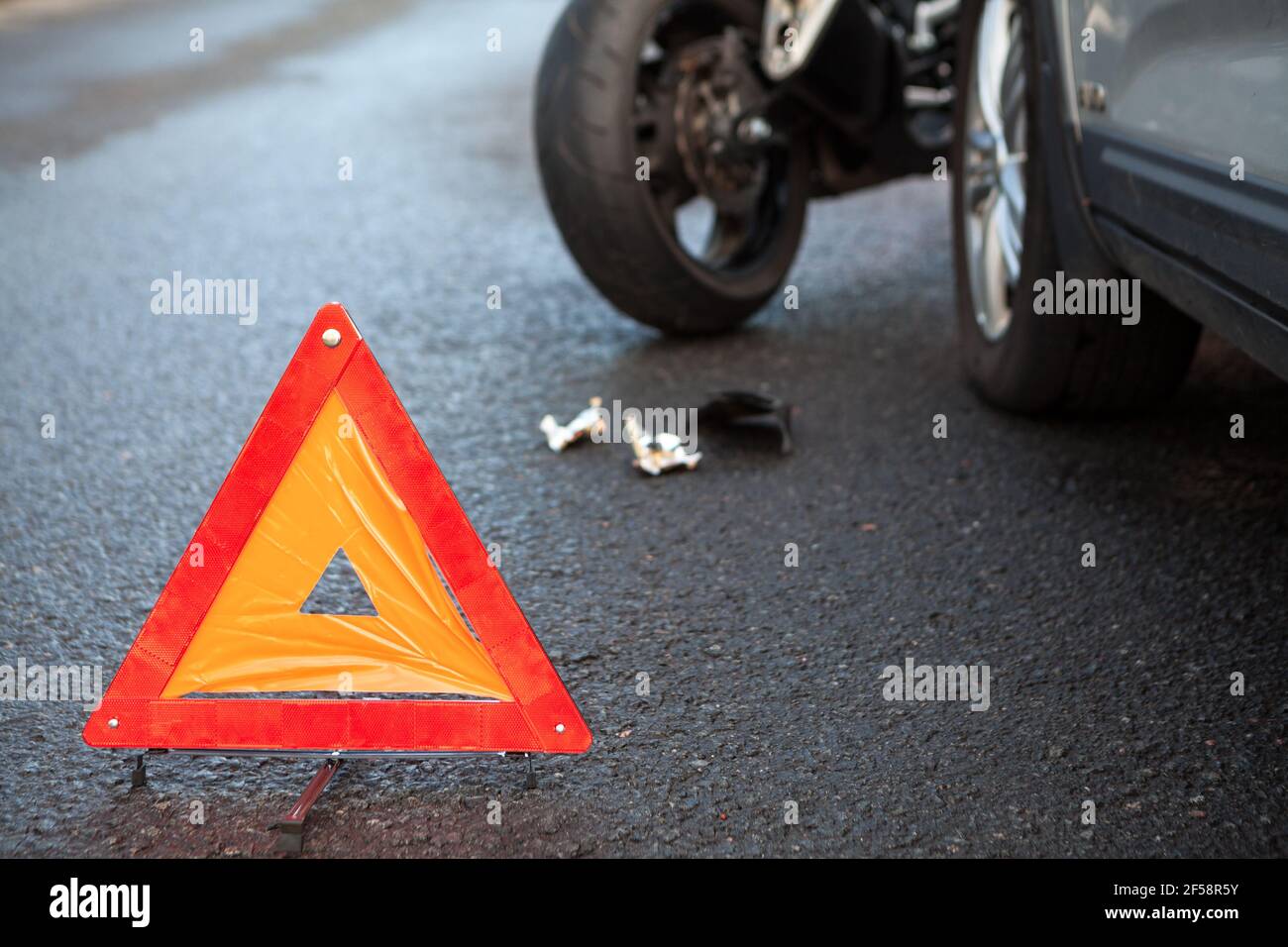 Emergency warning triangle positioned on asphalt road due accident with motorcycle and car Stock Photo