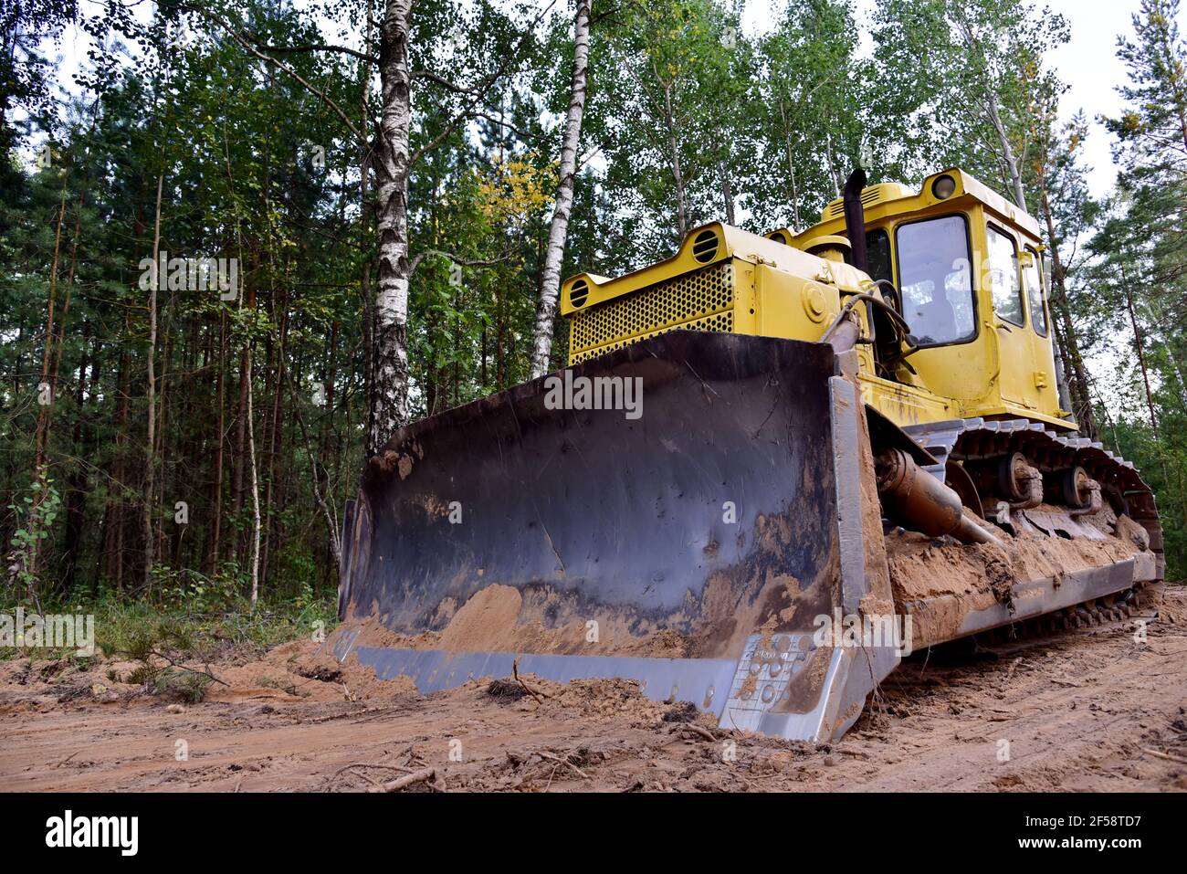 Dozer during clearing forest for construction new road . Yellow Bulldozer at forestry work Earth-moving equipment at road work, land clearing, grading Stock Photo